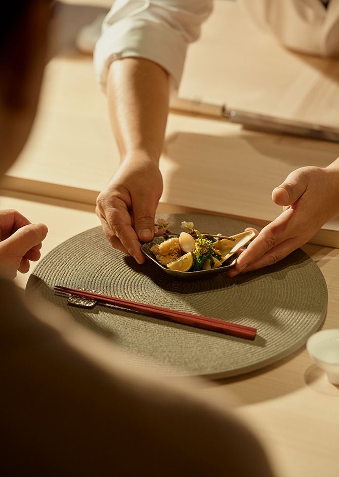 Gourmet dish being served at elegant table setting with red chopsticks and warm ambient lighting.